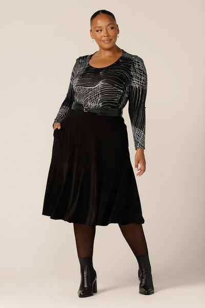 A plus size woman wears a long sleeve, round neck top with abstract black and white pattern, size 18. This is the Leith Top by Australian and New Zealand women's clothing label, L&F, ad is worn with a flared, black skirt and belt A good top for work and weekend wear, tailored details enhance this top's stretchy, textured knit fabric.