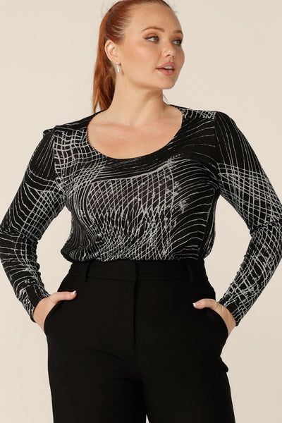 A curvy woman wears a long sleeve, round neck top in size 12. This is the Leith Top by Australian and New Zealand womenswear label, L&F, and is worn with a high waisted, tailored black work pants. A good top for work and weekend wear, tailored details enhance the black and white patterned, textured knit fabric of this women's top.