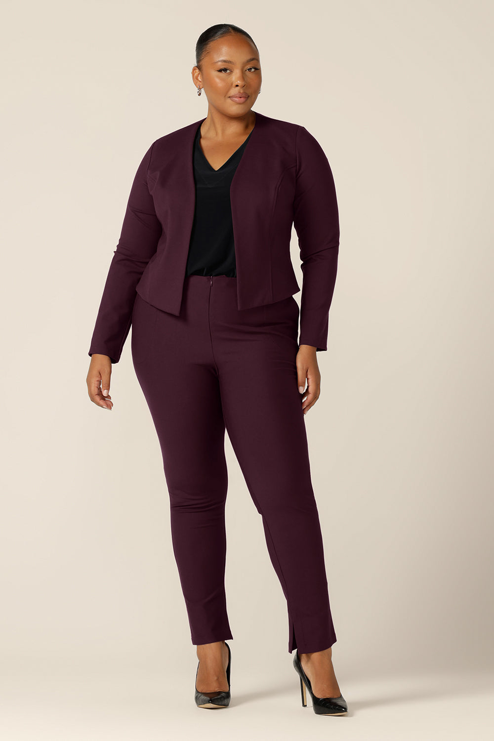 A good workwear jacket for fuller figure women, the Mackenzie Jacket in Mulberry is available to shop in sizes 8 to 24. Made in Australia by Australian and New Zealand women's clothing label, L&F, this work jacket is a collarless and open fronted with long sleeves and an angled hem. This corporate jacket is worn with slim leg pants and a black, V-neck top.