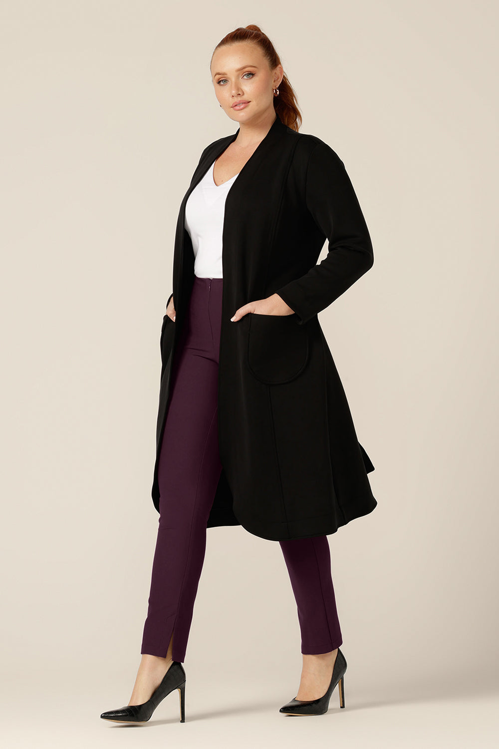 A curvy size 12 woman wears a softly tailored black trenchcoat in modal fabric by Australian and New Zealand women's clothing brand, L&F. Worn with mulberry slim leg pants and a white bamboo jersey top, this is a great coat for winter layering and travel.