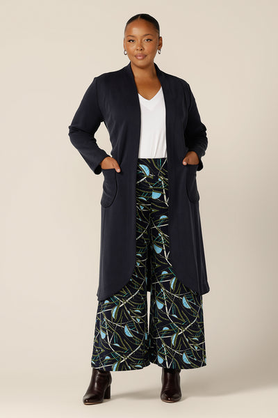 A size 18, fuller figure woman wears the Marant Trenchcoat in Bluestone by Australian and New Zealand size inclusive clothing brand, L&F. A collarless, open fronted coat with tie belt and patch pockets, this navy coat is worn with a white bamboo jersey top and wide leg, printed pants.