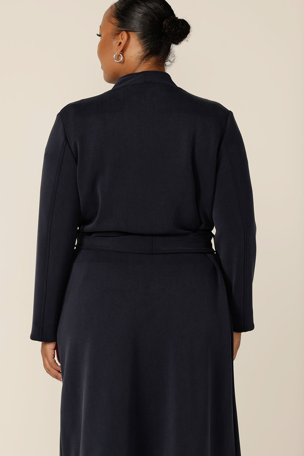 Back view of a size 18, plus size woman wearing the Marant Trenchcoat in Bluestone by Australian and New Zealand size inclusive clothing brand, L&F. A collarless, with tie belt at the waist and patch pockets is an easy coat for winter layering.