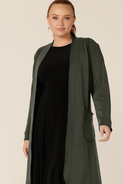 A classic winter coat for women, the Marant Trenchcoat in Sage green by Australian and New Zealand women's clothing brand, L&F is shown in a size 12, and worn with a black jersey dress. A collarless, open fronted coat with tie belt and patch pockets, this women's winter coat is available to shop in an inclusive 8 to 24 size range.