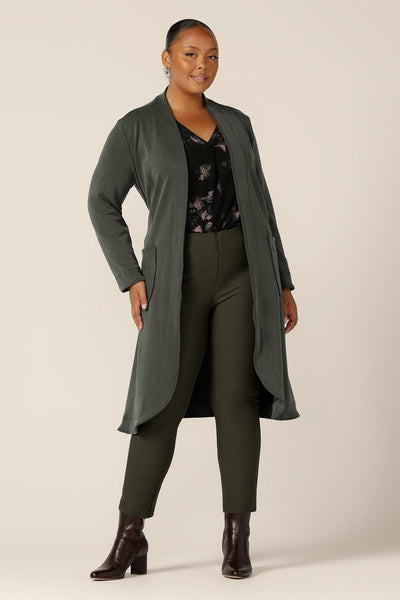 A classic winter coat for women, the Marant Trenchcoat in Sage green by Australian and New Zealand women's clothing label L&F is shown in a size 18, and worn with a printed, black jersey top and olive green, slim leg trousers. A soft tailoring coat, this collarless, open fronted jacket with tie belt and patch pockets, is available to shop for women in sizes 8 to 24.