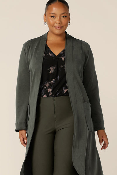 A classic winter jacket for women, the Marant Trenchcoat in Sage green by Australian and New Zealand women's clothing brand L&F is shown in a size 18 for fuller figure women, and worn with a printed, black jersey top and olive green, slim leg pants. A collarless, open fronted coat with tie belt and patch pockets, this warm winter jacket is available to buy in an inclusive 8 to 24 size range.
