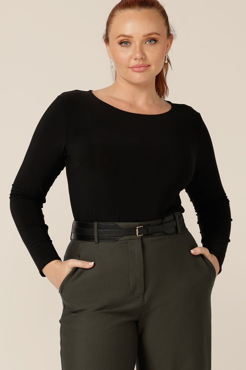 A women's, long sleeve, boat neck top in black jersey worn with tailored, olive green pants and a black belt. Made in Australia by Australian and New Zealand women's clothing brand, L&F, this is an easy workwear top for women in petite to plus sizes.