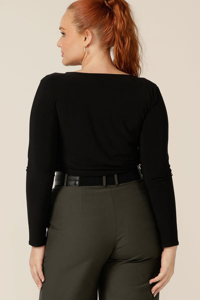 Back view of a women's, long sleeve, boat neck top in black jersey worn with tailored, olive green pants and a black belt. Made in Australia by Australian and New Zealand women's fashion label, L&F, this is an easy workwear top for women in sizes 8 to 24.