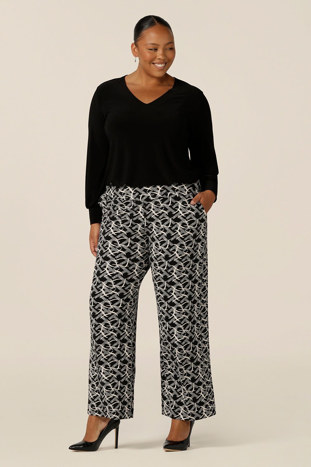 A plus size, size 18 woman wears wide leg, pull on pants with a deep waistband in black and white jersey. Worn with a long sleeve black top, these easy care pants are great for work and corporate wear.