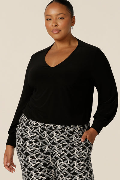 A plus size, size 18 woman wears a V-neck black top with long sleeves. This long sleeved top features cuffs at the wrists and a shirttail hemline. Made in Australia by Australian and New Zealand women's clothing label, L&F.