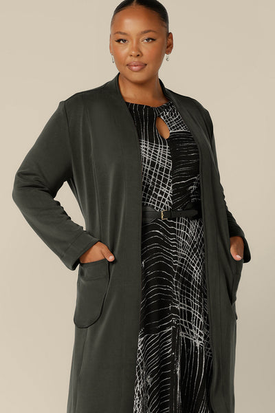 A classic winter coat for women, the Marant Trenchcoat in Sage green by Australian and New Zealand women's clothing label L&F is shown in a size 18, and worn with a printed, knit jersey dress. A collarless, open fronted coat with tie belt and patch pockets, this women's winter jacket is available online in sizes 8 to 24.