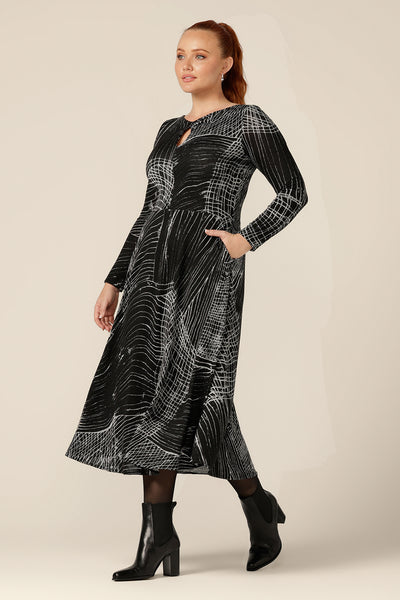 Side view of a curvy woman wearing a midi length, long sleeve dress in size 12, with twisted keyhole detail and side pockets. Made by Australian and New Zealand women's clothing brand, L&F in an inclusive size range of sizes 8 to 24.