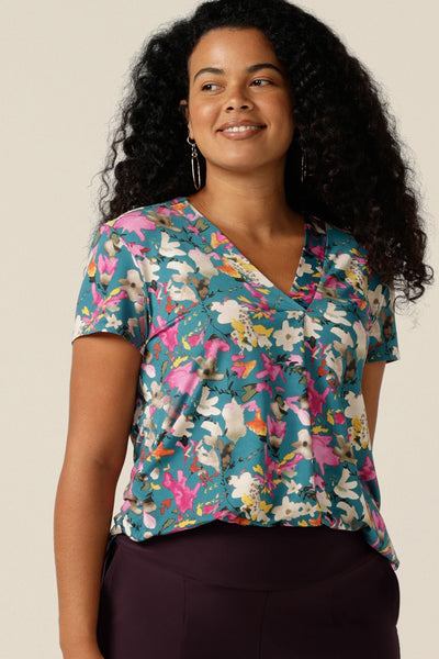 Size 12 curvy woman wearing a semi-fitted V-neck top with short sleeves. The top is shown in floral print slinky jersey for a feminine work wear style and smart-casual business dress or weekend wear. The jersey top is made in Australia by petite-to-plus-size clothing experts, Leina and Fleur