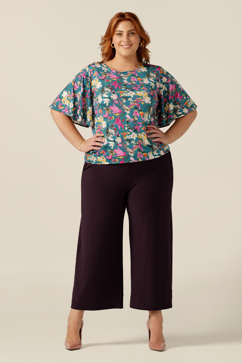 Curvy woman wearing a floral print jersey top with flutter sleeves. The top is made in Australia by Leina and Fleur, who specialise in quality tops, dresses and pants for petite to plus size women for work, travel and casual wear.