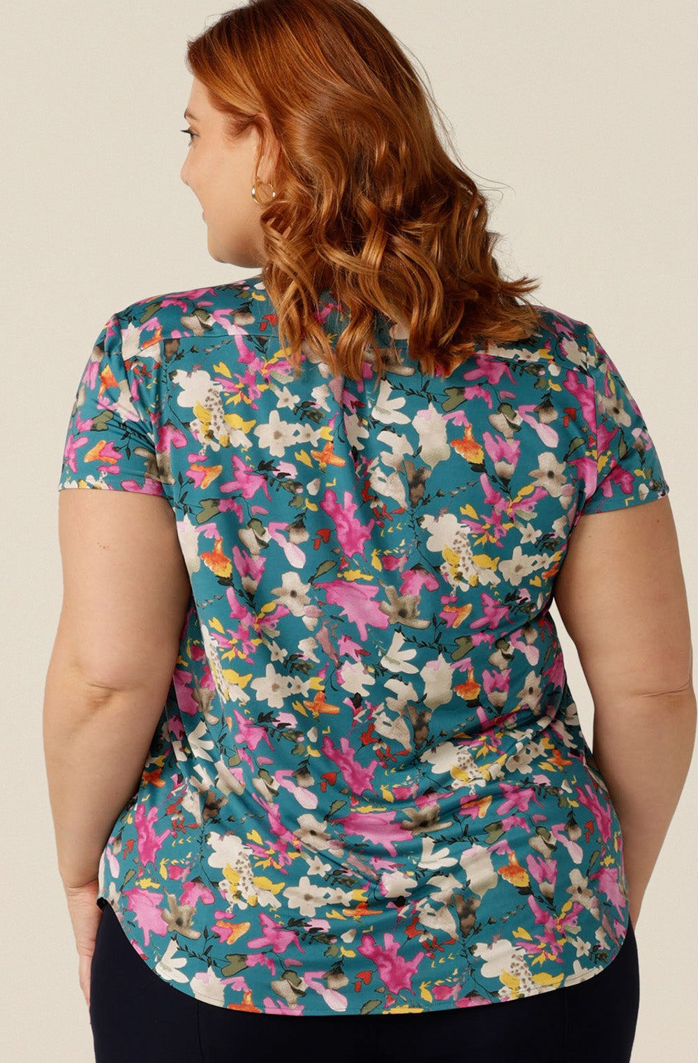 Size 18 curvy woman wearing a semi-fitted V-neck top with short sleeves. The top is shown in floral print slinky jersey for a feminine work wear style and smart-casual business dress or weekend wear. The jersey top is made in Australia by petite-to-plus-size clothing experts, Leina and Fleur
