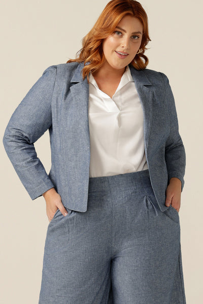 size 18 woman wearing a soft tailored jacket in cotton-linen blend Chambray fabric. The jacket is open-fronted and has long sleeves. This jacket is styled with a white shirt and matching Chambray tailored, cropped-length pants to give a work wear look. Jacket, shirt and pants are made in Australia for petite to plus size women.