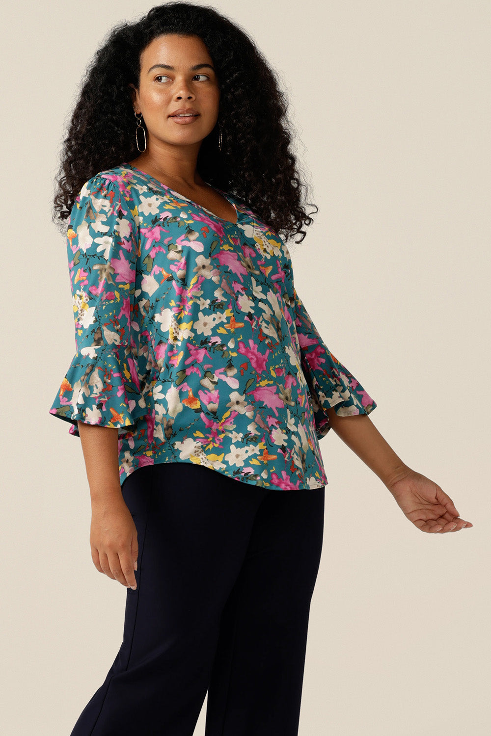 a size 12 curvy woman wearing a semi-fitted jersey top. The top features 3/4 sleeves with fluted cuffs, a V-neck and  a floral print. The top was made in Australia in petite to plus sizes by women's clothing brand, Leina and Fleur
