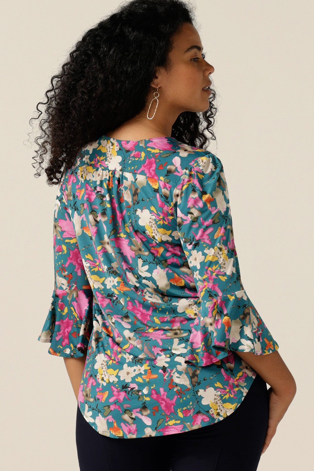 a size 12 curvy woman wearing a semi-fitted jersey top. The top features 3/4 sleeves with fluted cuffs, a V-neck and  a floral print. The top was made in Australia in petite to plus sizes by women's clothing brand, Leina and Fleur