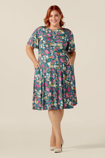 size 18 curvy woman wearing a reversible fixed wrap jersey dress. The reversible nature of the dress allows for wear as a wrap-style dress or as a boat-neck dress. Also featuring short flutter sleeves, a knee length skirt and pockets, this dress is designed to flatter petite to plus size women. Made in Australia by women's work wear clothing label, Leina and Fleur 