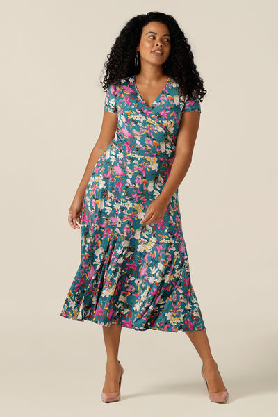 A woman wearing a fixed wrap jersey dress with short sleeves and a floral print. The dress features a maxi-length skirt with pockets. Made in Australia by women's clothing brand L&F, this wrap dress fits petite to curvy women.