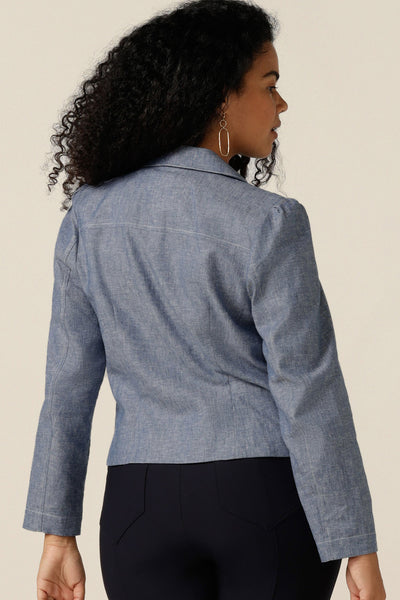 A size 12 curvy woman wears a softly tailored jacket in cotton-linen blenc Chambray fabric. the jacket is open-fronted and has long sleeves. Under the jacket, the woman wears a red bamboo jersey top with round neck, and black trousers. The jacket is styled as a smart-casual cover-up for weekend and going out fashion.