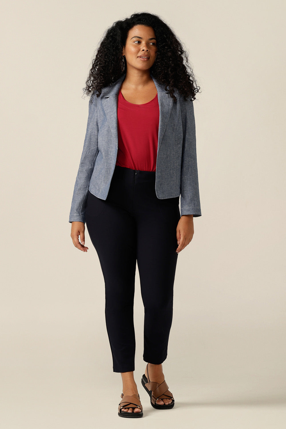 A size 12 curvy woman wears a softly tailored jacket in cotton-linen blenc Chambray fabric. the jacket is open-fronted and has long sleeves. Under the jacket, the woman wears a red bamboo jersey top with round neck, and black trousers. The jacket is styled as a smart-casual cover-up for weekend and going out fashion.