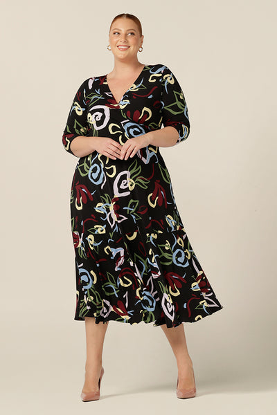 A size 18, fuller figure woman wears a reversible wrap dress with 3/4 sleeves and midi-length skirt with ruffle hem. A reversible dress style, this dress wears with a V-neckline, wrap front or a high boat neckline for workwear or event wear.