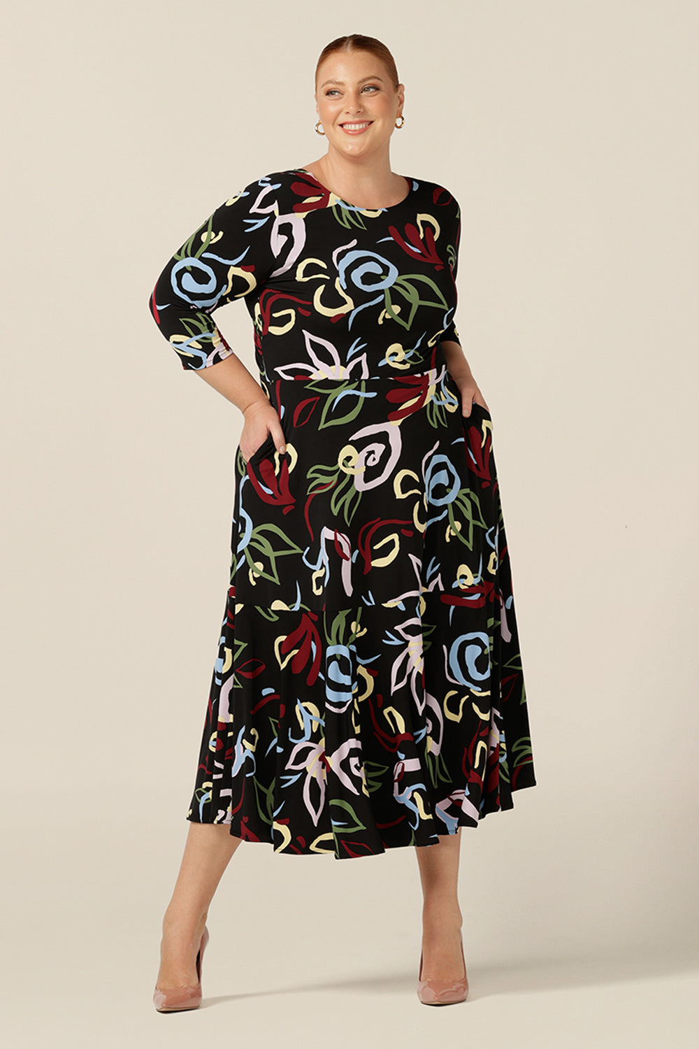 Wearing a reversible dress for women, this size 18, fuller figure woman styles it as boat neck dress. Featuring 3/4 sleeves and full midi-length skirt with ruffle hem, this dress has a black-base print for easy styling for work and corporate wear. 