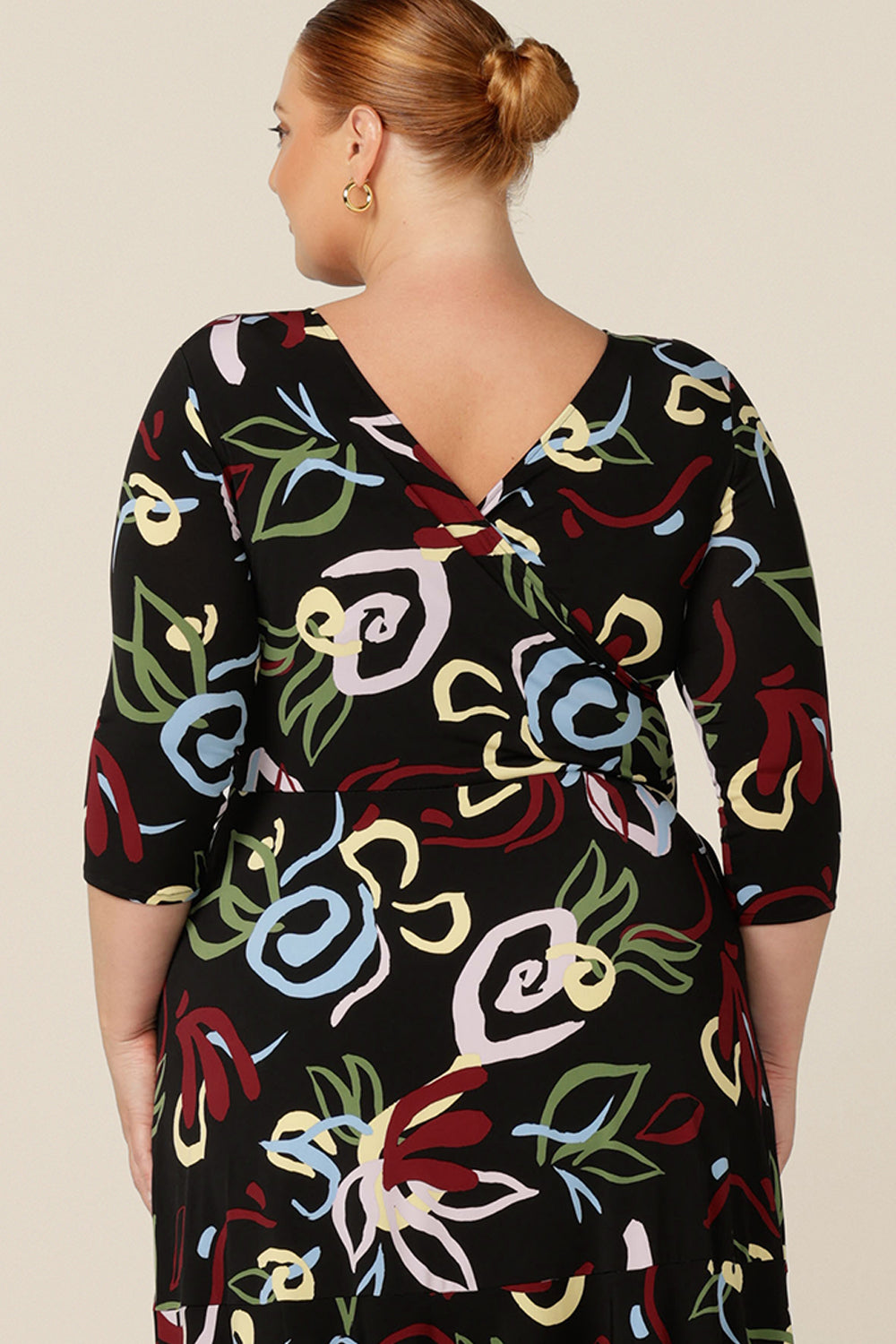 Back view of a reversible fixed wrap dress worn as a boat neck with a V back. Designed for work and corporate wear, this printed dress has a black base for easy styling with workwear separates.