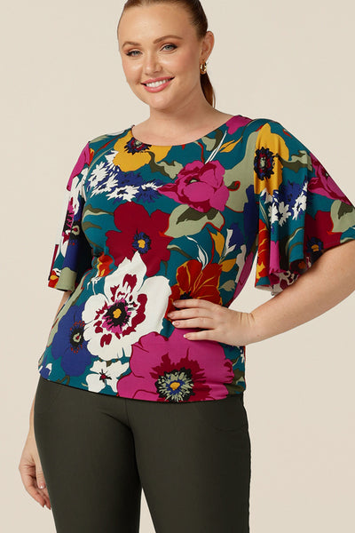 A curvy size 12 woman wears a round neck jersey top with short flutter sleeves. Made in Australia, this floral print top is good for work or casual wear.