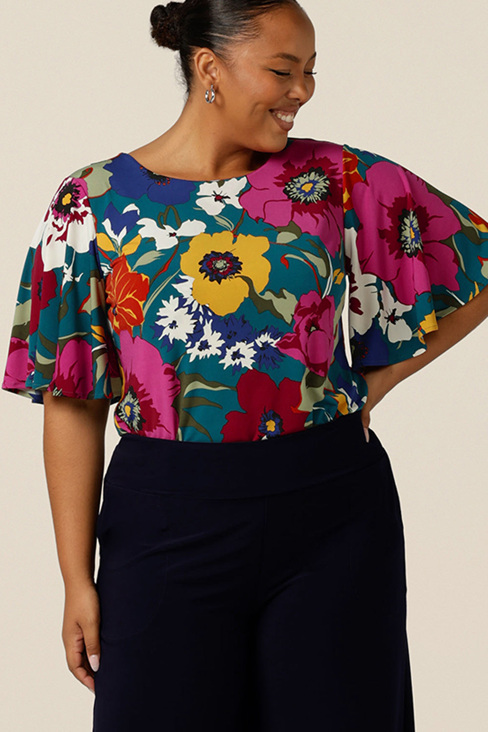 A fuller figure, size 18 woman wears a round neck jersey top with wide flutter sleeves. Made in Australia, this quality workwear top gives feminine style to corporate pants and skirts. Available in an inclusive 8-24 size range.