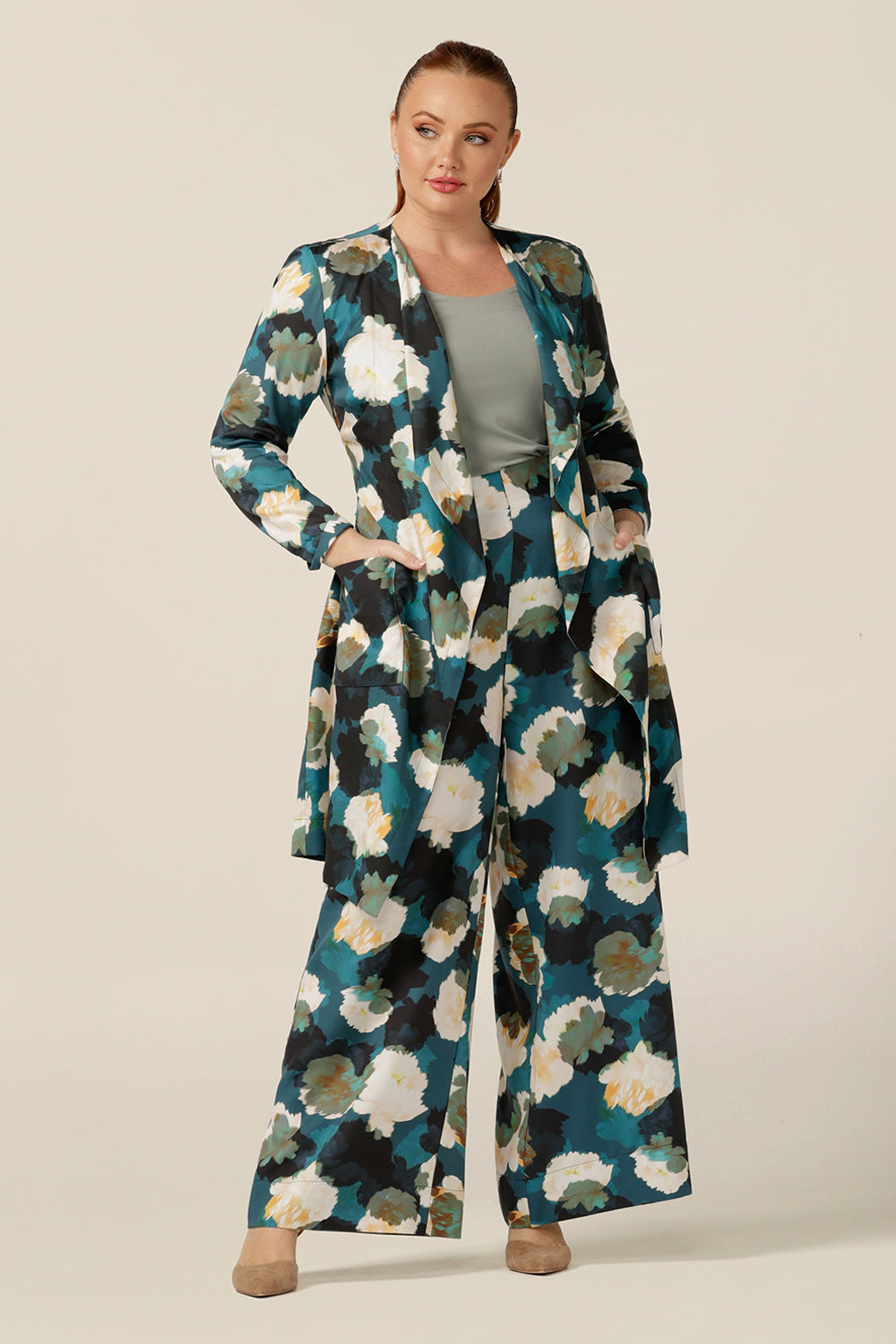 a size 12, plus size woman wears a soft trench coat-style jacket with waterfall front, patch pockets and belt tie. Sustainably-made in Australia, this luxury knee-length jacket is worn wide printed wide-leg pants and a bamboo jersey top.