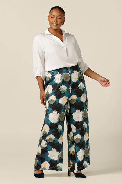 A size 18, plus size woman wears high-waisted printed wide-leg pants. Made in Australia from sustainable Tencel fabric, these eco-conscious trousers are part of women's clothing brand, elarroyoenterprises's focus on sustainable fashion. Worn with a white eco-conscious shirt to complete the corporate look.