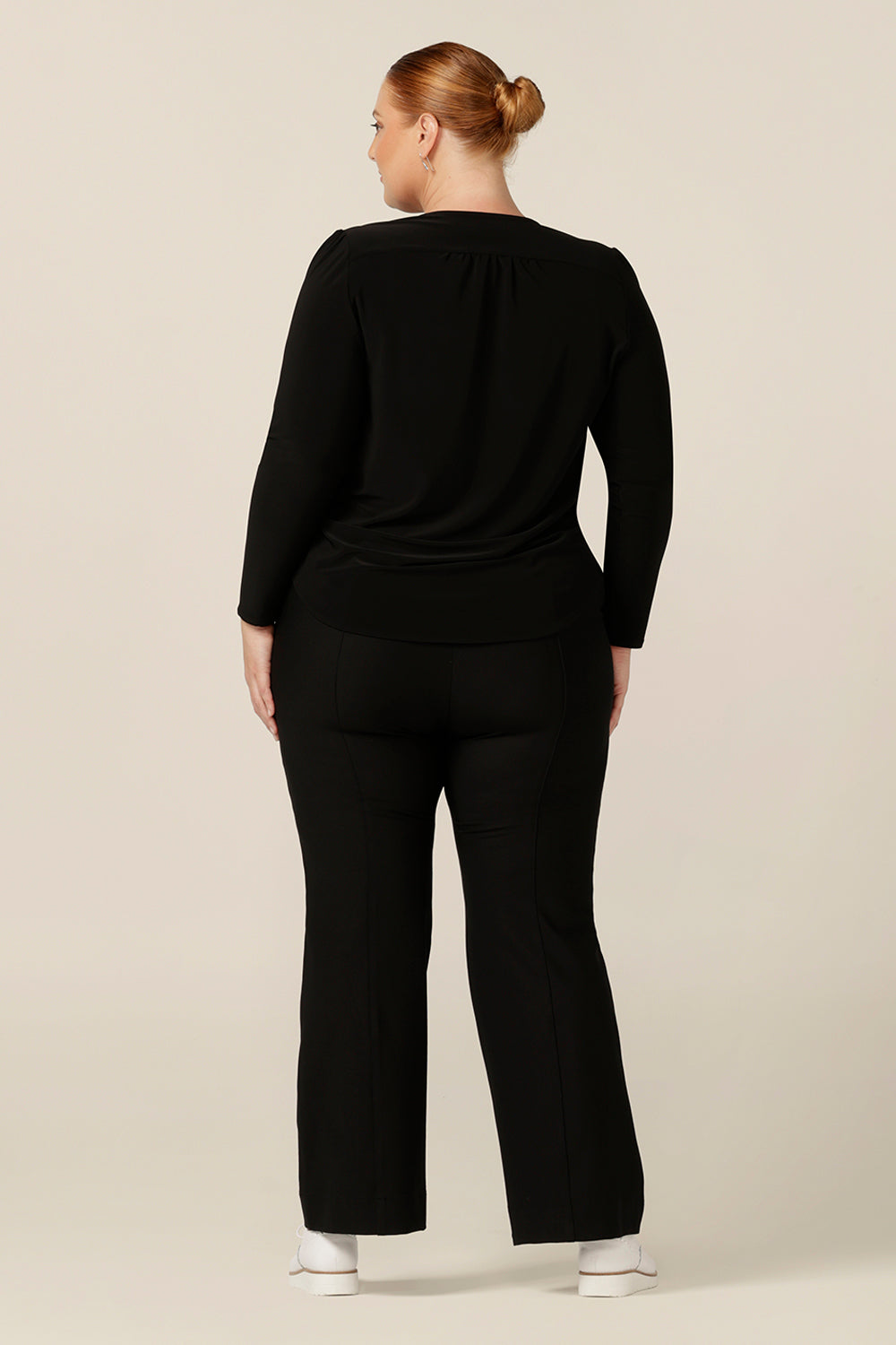 Back view of a size 18, fuller figure woman wearing a long sleeve, V neck top in black jersey. Worn with black bootleg pants, this is a comfortable top for work or casual wear and, made in Australia it comes with quality assurance.