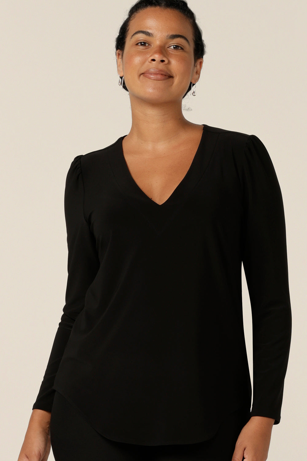 A size 12, curvy woman wears a long sleeve, V neck top in black jersey. A comfortable top for work or casual wear, this classic women's top is made in Australia by Australia and New Zealand women's clothing company.