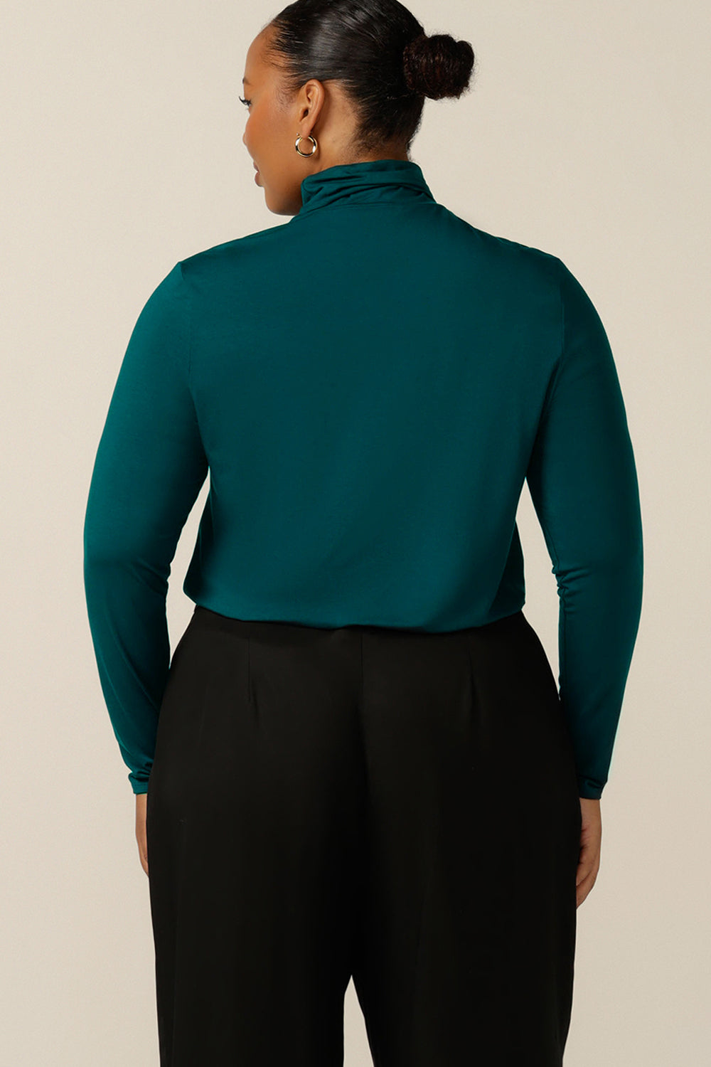 Back view of an Australian-made, women's long-sleeve, turtle neck top in petrol green bamboo jersey. Worn by a size 18, plus size woman, this polo neck top is available in an inclusive 8-24 size range. 
