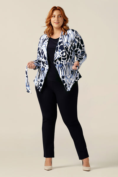 A size 18, plus size woman wears a comfortable work jacket in navy and white. Open-fronted, this soft tailored jacket has a tie belt and long sleeves. Worn with slim-leg navy pants, this jacket is a good workwear jacket for corporate and smart-casual business wear.