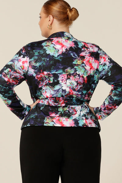 Back view of a size 18, fuller figure woman wearing a comfortable work jacket in abstract floral print on a black base. This soft tailoring jacket has a tie belt, soft collar and long sleeves. Made in Australia in sizes 8-24, shop this work jacket with free shipping to New Zealand.