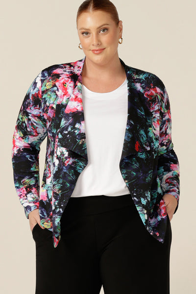 A size 18, fuller figure woman wears a comfortable work jacket in abstract floral print on a black base. This soft tailoring jacket has a tie belt, soft collar and long sleeves. Worn with black pants and a white T-shirt, this is a pretty jacket for work or weekend wear. Shop with free shipping to New Zealand..