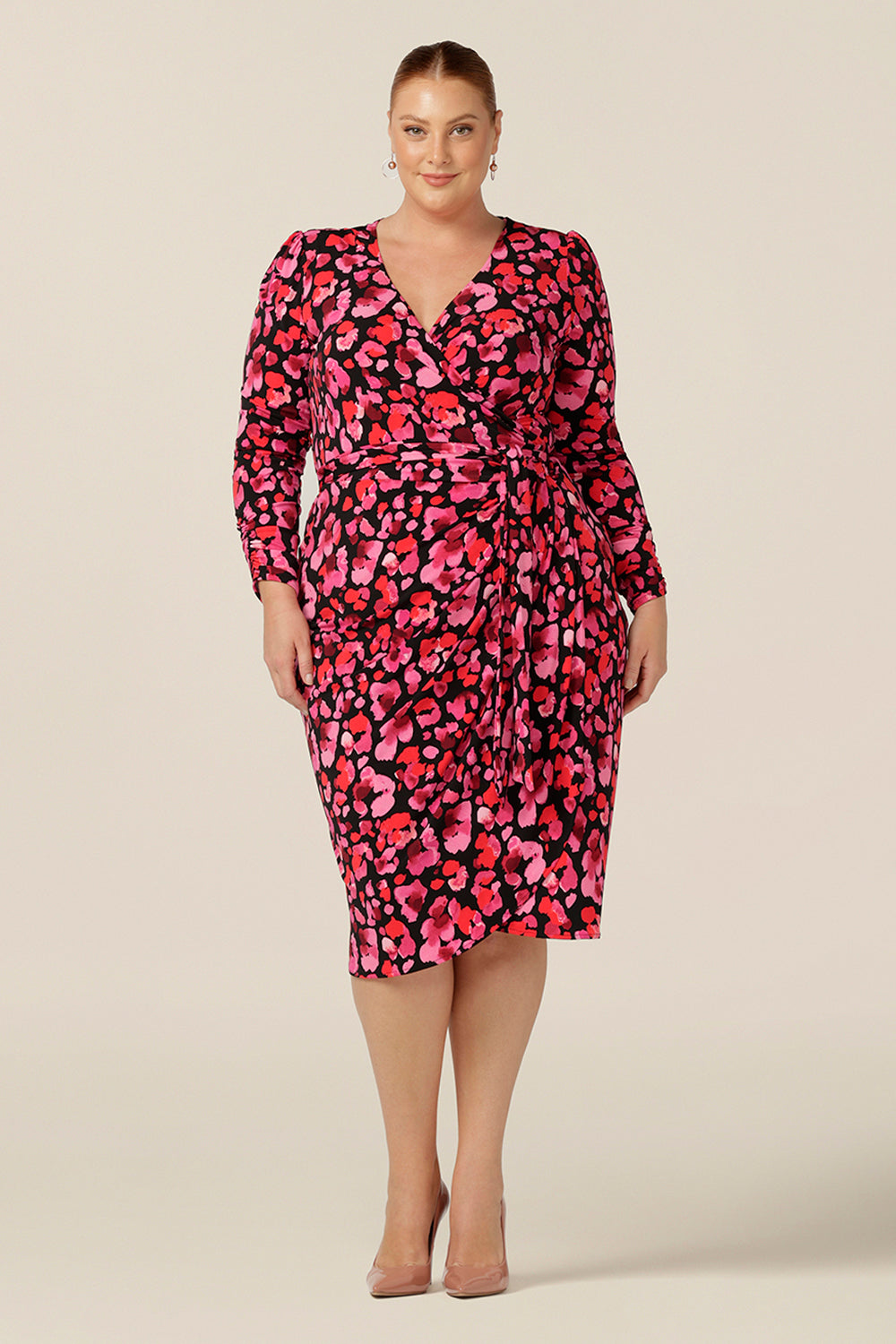 A fuller figure, size 18 woman wears a jersey wrap dress with long sleeves and a tulip skirt. Made in Australia and available to shop online in Australia and New Zealand, this wrap dress can be worn for workwear or as a going out dress for date night style. 