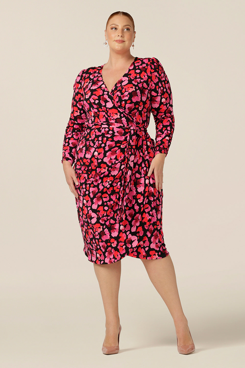 A fuller figure, size 18 woman wears a jersey wrap dress with long sleeves and a tulip skirt. Made in Australia and available to shop online in Australia and New Zealand, this wrap dress can be worn for corporate wear or as a occasion dress for date night style.