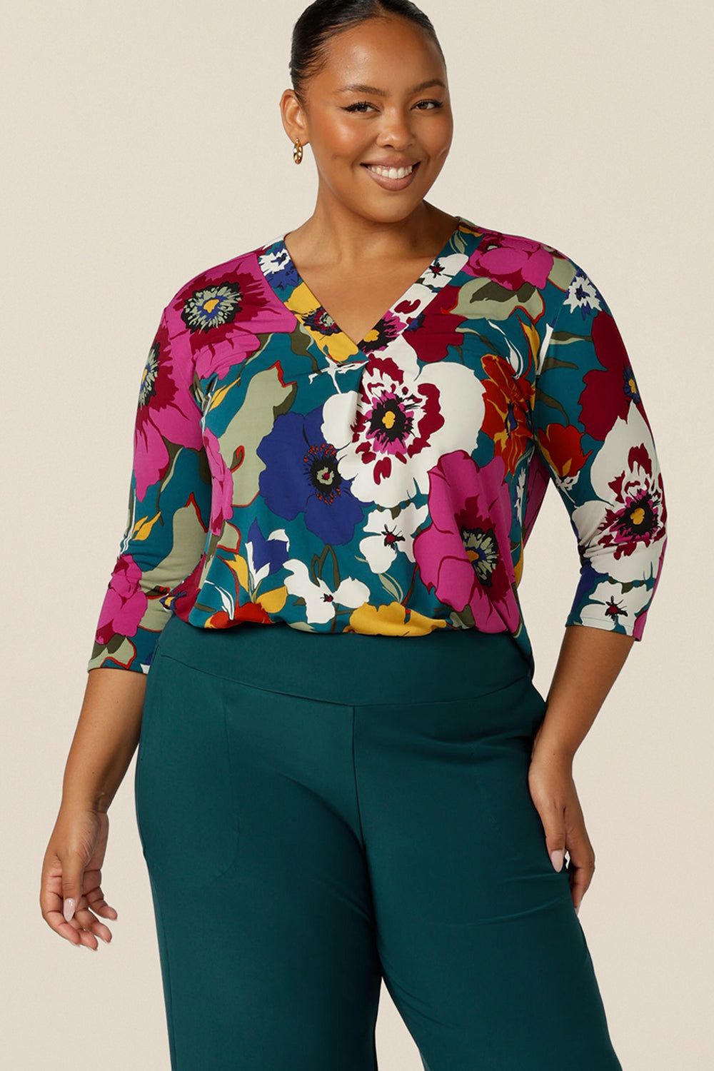A size 18, fuller figure woman wears a jersey, V-neck top with 3/4 sleeves. A tailored top for work and corporate wear, here the floral print top is show with wide-leg trousers.