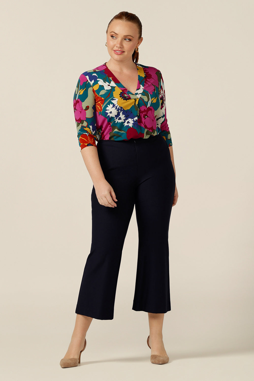 A curvy size 12 woman wears a jersey, V-neck top with 3/4 sleeves tucked in to cropped, flared leg, navy blue work pants. Made-in Australia, this tailored top for work and corporate wear is available in an inclusive 8-24 size range.