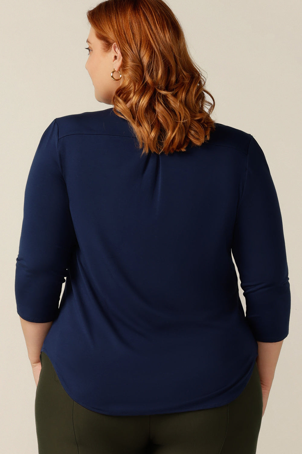 a woman wears a navy blue bamboo jersery top with a round neckline, 3/4 and back pleat detail. In a size 18, this plus size top shows Australian clothing label, L&Fs inclusive size range which make tops for petite to plus size women to buy..