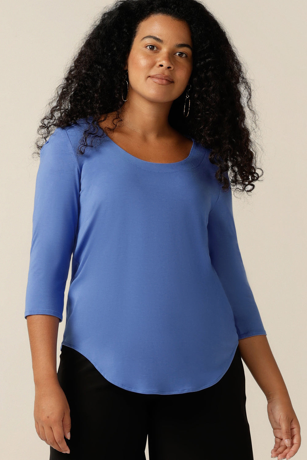 A curvy size 12 woman wears a blue bamboo jersey top. The top has a round neckline, 3/4 sleeves, and a curved shirttail hemline. A top made from sustainable natural fibres, it is a lightweight, breathable top that's made in Australia.