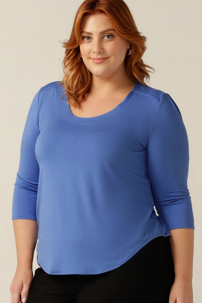 A plus size, size 18 woman wears a blue bamboo jersey top. The top has a round neckline, 3/4 sleeves, and a curved shirttail hemline. Wear this women's jersey top untucked as a comfortable, casual top or tucked with tailored pants as a workwear top. 