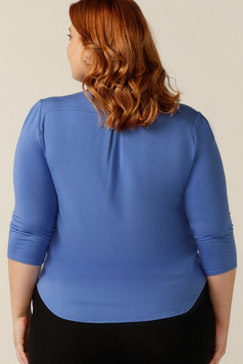 A plus size, size 18 woman wears a blue bamboo jersey top. The top has a round neckline, 3/4 sleeves, and a curved shirttail hemline. Made in bamboo jersey, this top is made from sustainable, natural fibres that are lightweight and breathable and part of the movement towards eco-conscious fashion.