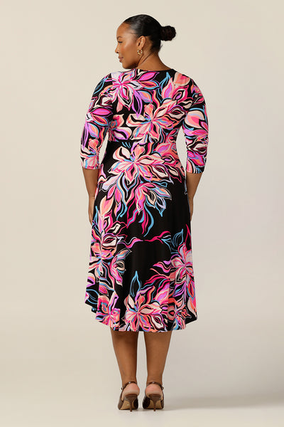  A size 18 woman wears a bright-coloured floral print jersey dress by Australian and New Zealand women's clothing label, L&F. this empire line dress features a V-neckline with twist detail, 3/4 sleeves and a full below-the-knee-length skirt. Made in Australia, this is a dress for work and corporate dressing as well as a good dress for events and occasion wear.