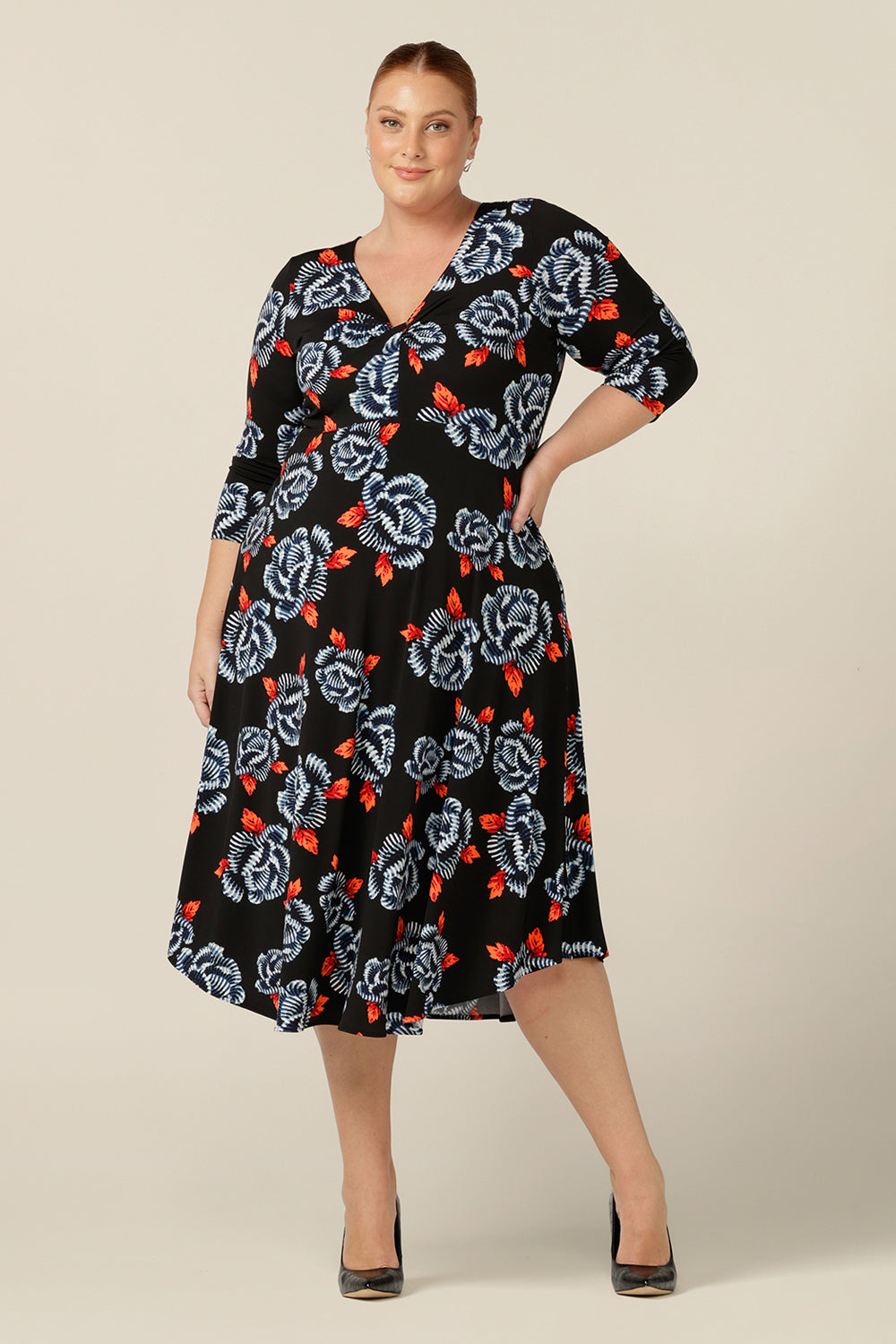 A size 18 fuller figure woman wears a blue and orange floral print jersey dress by Australian and New Zealand women's clothing brand, L&F. this empire line dress features a V-neckline with twist detail, 3/4 sleeves and a full below-the-knee-length skirt. Australian-made, shop L&F work dresses in sizes 8 to size 24.