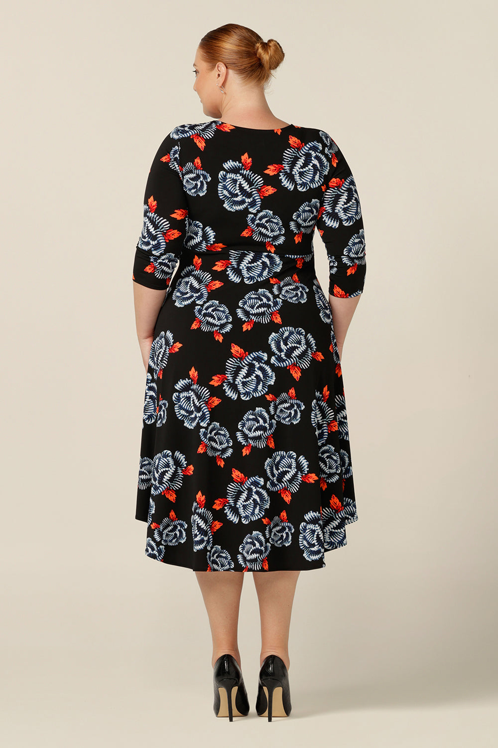 Back view of a size 18 fuller figure woman wears a blue and orange floral print jersey dress by Australian and New Zealand women's clothing brand, L&F. this empire line dress features a V-neckline with twist detail, 3/4 sleeves and a full below-the-knee-length skirt. Australian-made, shop L&F workwear dresses in sizes 8 to size 24.