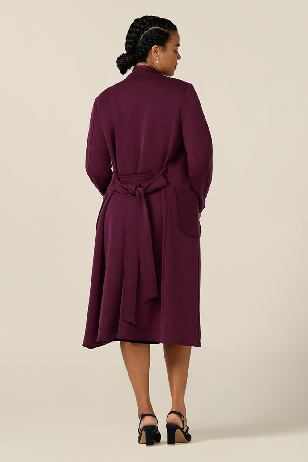 Back view of a size 12, curvy woman wearing a soft tailoring trenchcoat by Australia and New Zealand women's clothing label, L&F. In wine red Modal fabric, this light-weight winter coat is comfortable for layering over workwear and corporate suiting for winter work wear solutions.